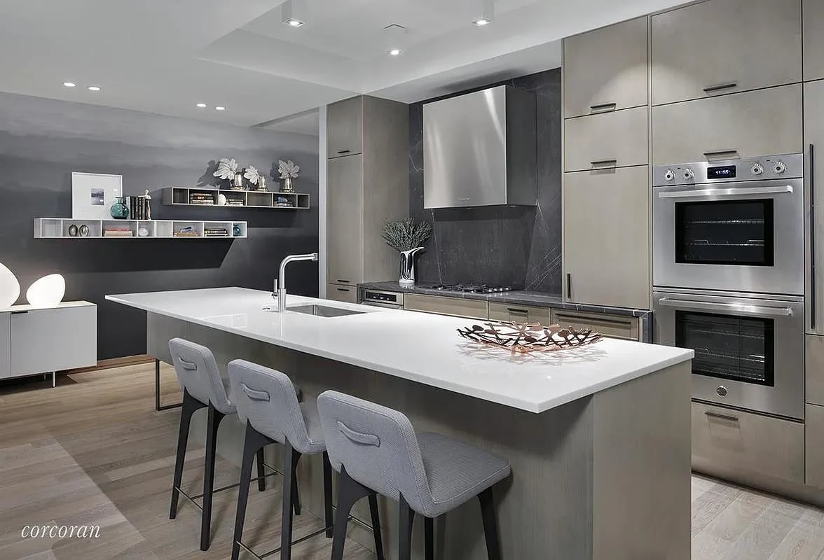 Modern kitchen with a long white island, three bar stools, dark stone backsplash, and double wall ovens.