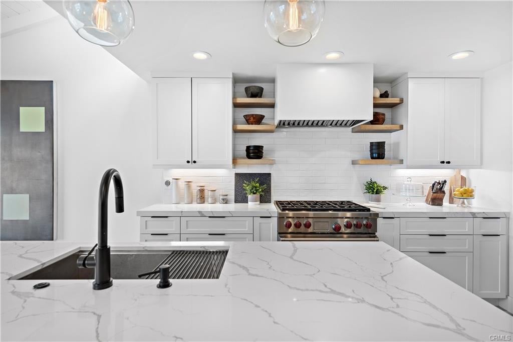 Modern white kitchen with a marble-veined island, black faucet, and stainless steel range.