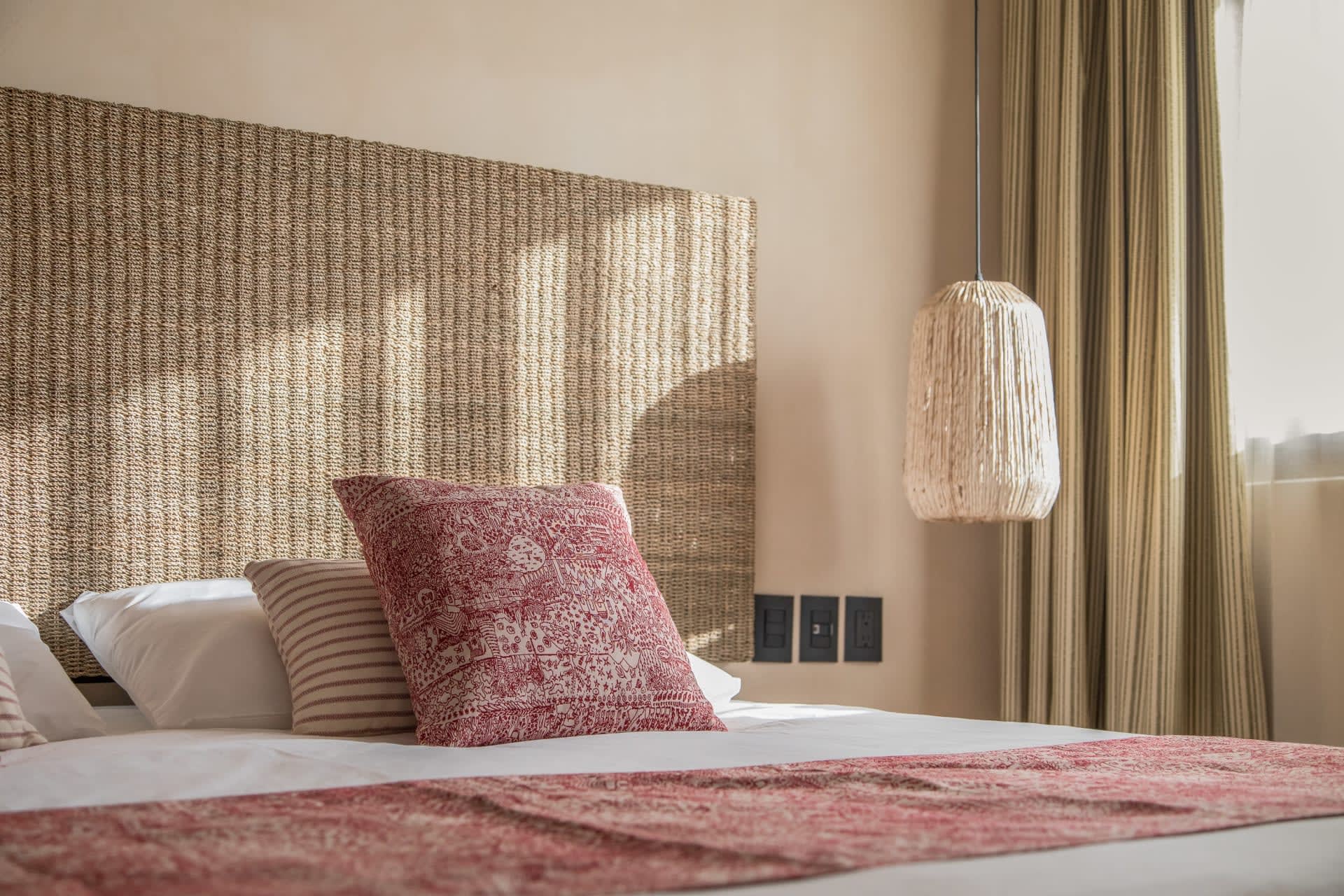 Bedroom with a woven headboard, red patterned pillows, and a pendant light.
