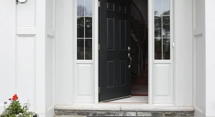 The entrance of a house with the front door slightly open, revealing a glimpse of the interior. The house has a clean and welcoming look.