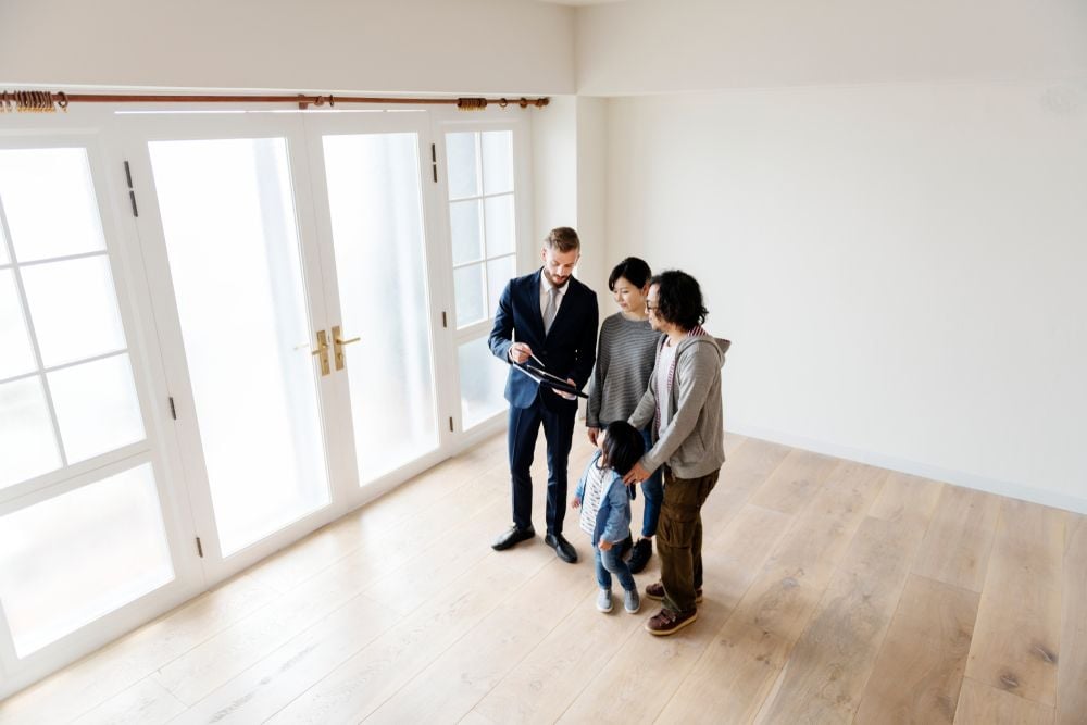 Agent shows a family an empty room with pale wood floors and French doors.