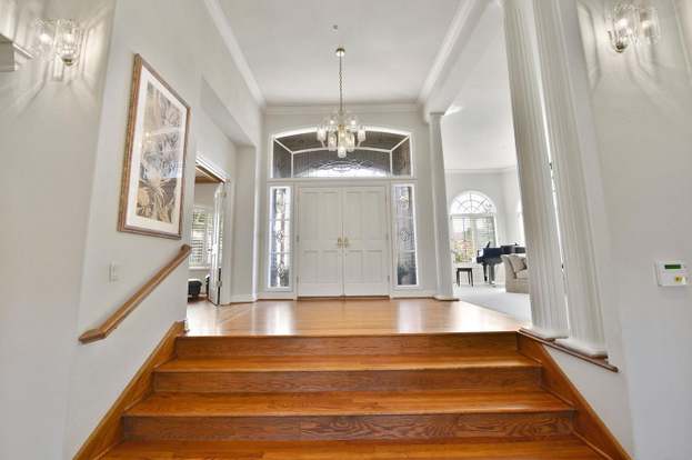 Entry foyer with polished wood stairs leading to double front doors and a chandelier.