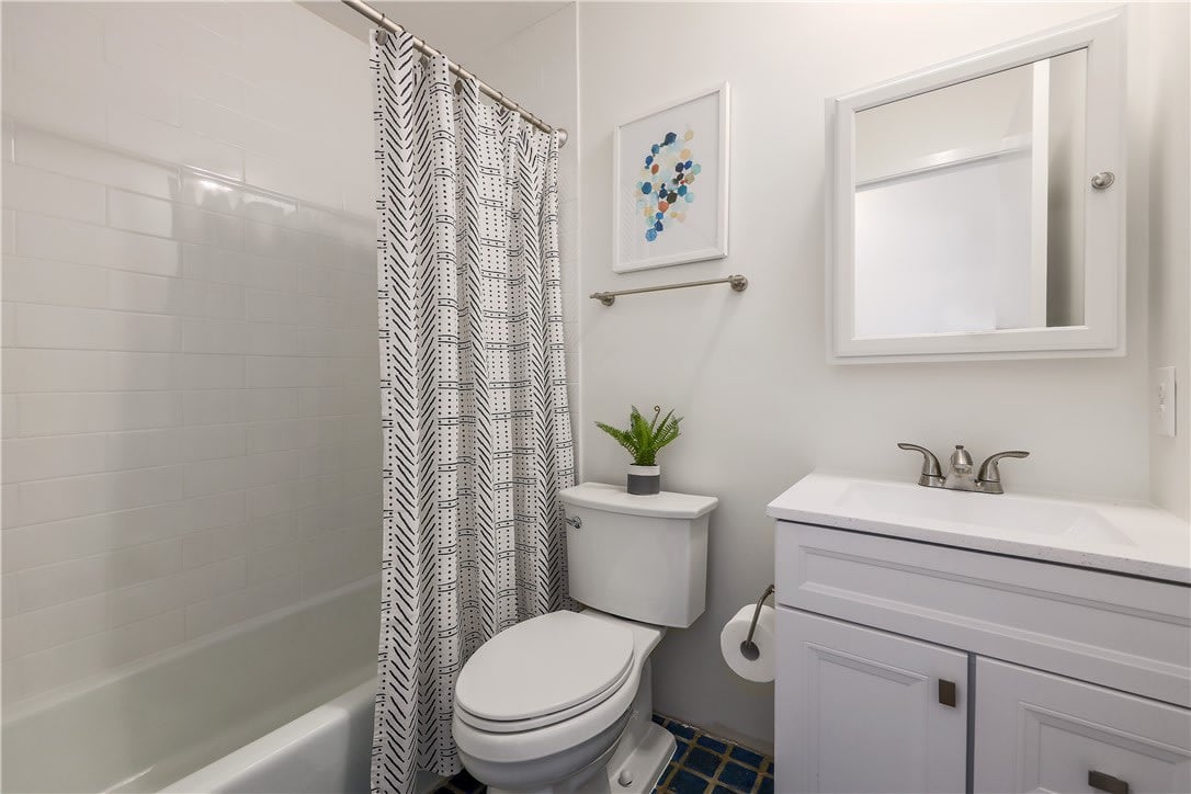 Bathroom with a white vanity, bathtub behind a patterned shower curtain, and blue tiled floor.