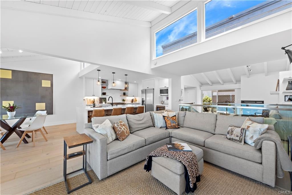 Open-plan living room with a gray sectional, vaulted ceiling, clerestory windows, and kitchen behind it.
