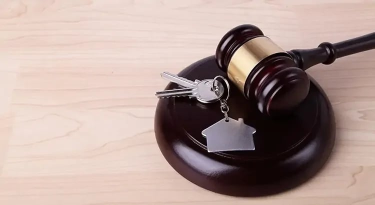 A gavel and a house key placed on a wooden surface. The image represents a legal or real estate transaction theme.