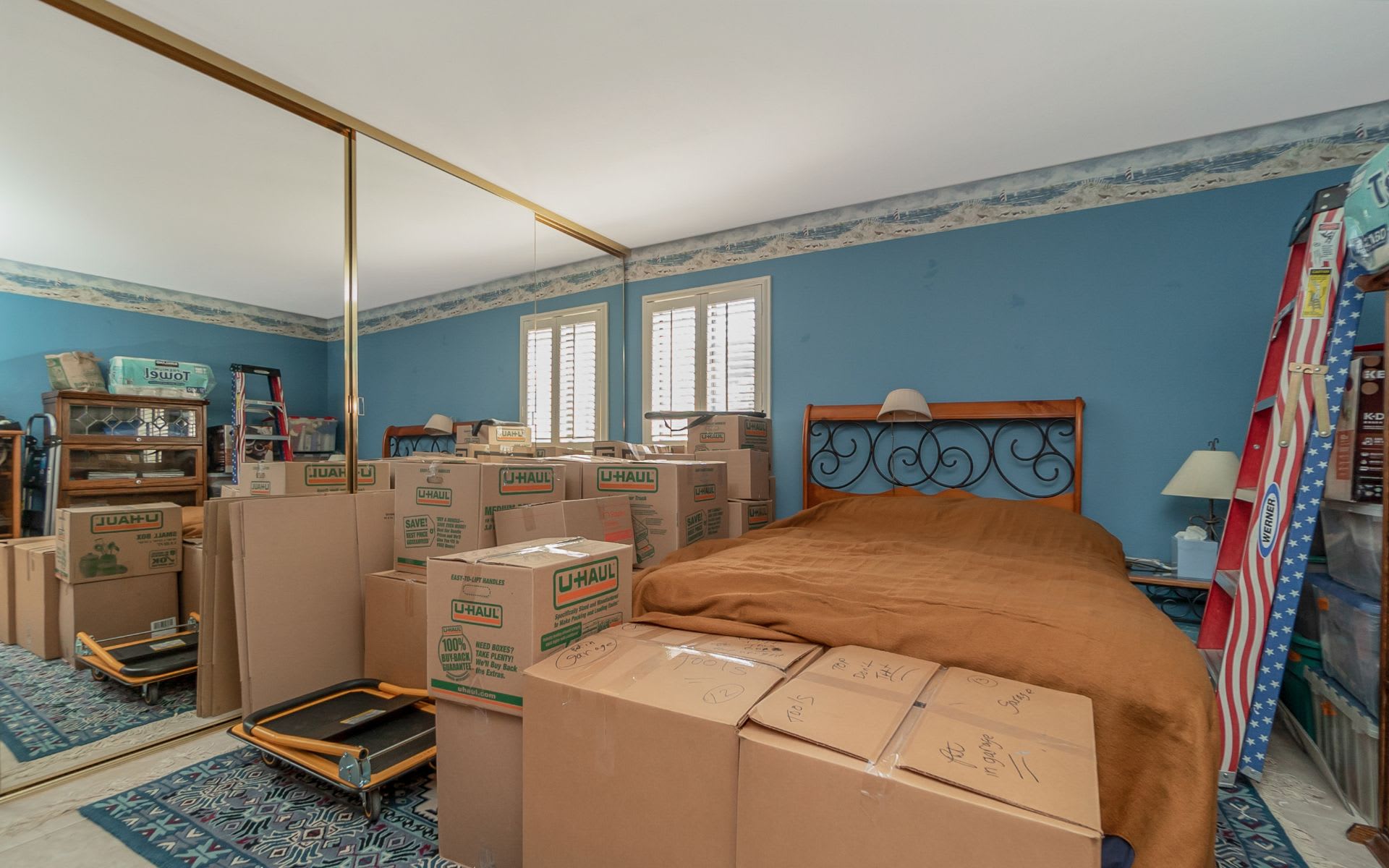 Bedroom with blue walls, a metal-headboard bed, and moving boxes filling the room.