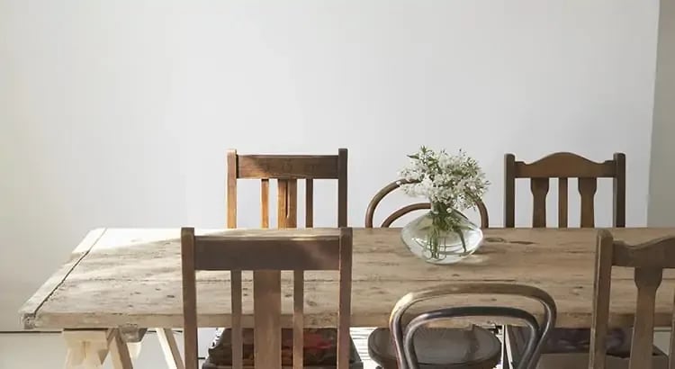 A dining room with a wooden table and chairs. The table is set with placemats and a vase with flowers, creating a cozy and inviting dining space.