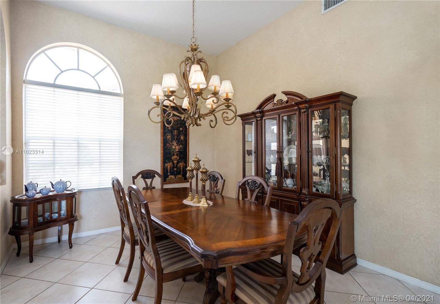 Dining room with a polished wooden table, glass-front china cabinet, and tall arched window.