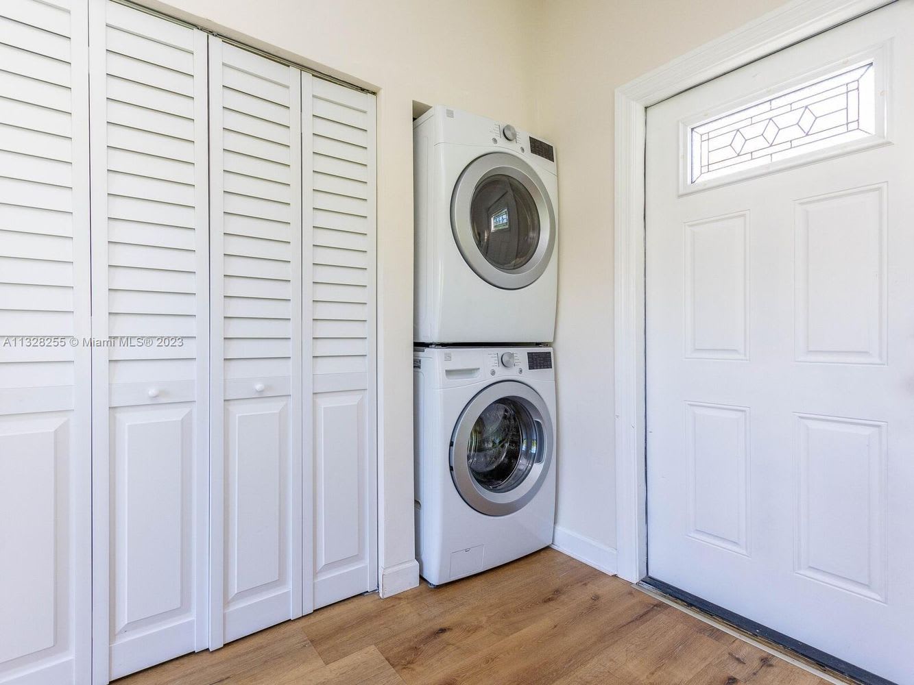Laundry area with stacked washer and dryer, white louvered cabinets, and a decorative glass door.