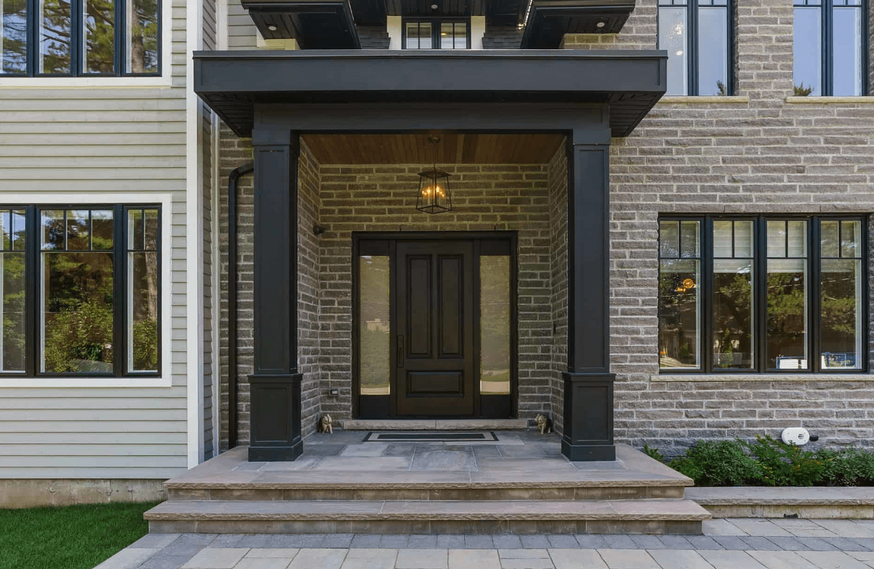 A cozy front porch of a brick house with a black door and windows