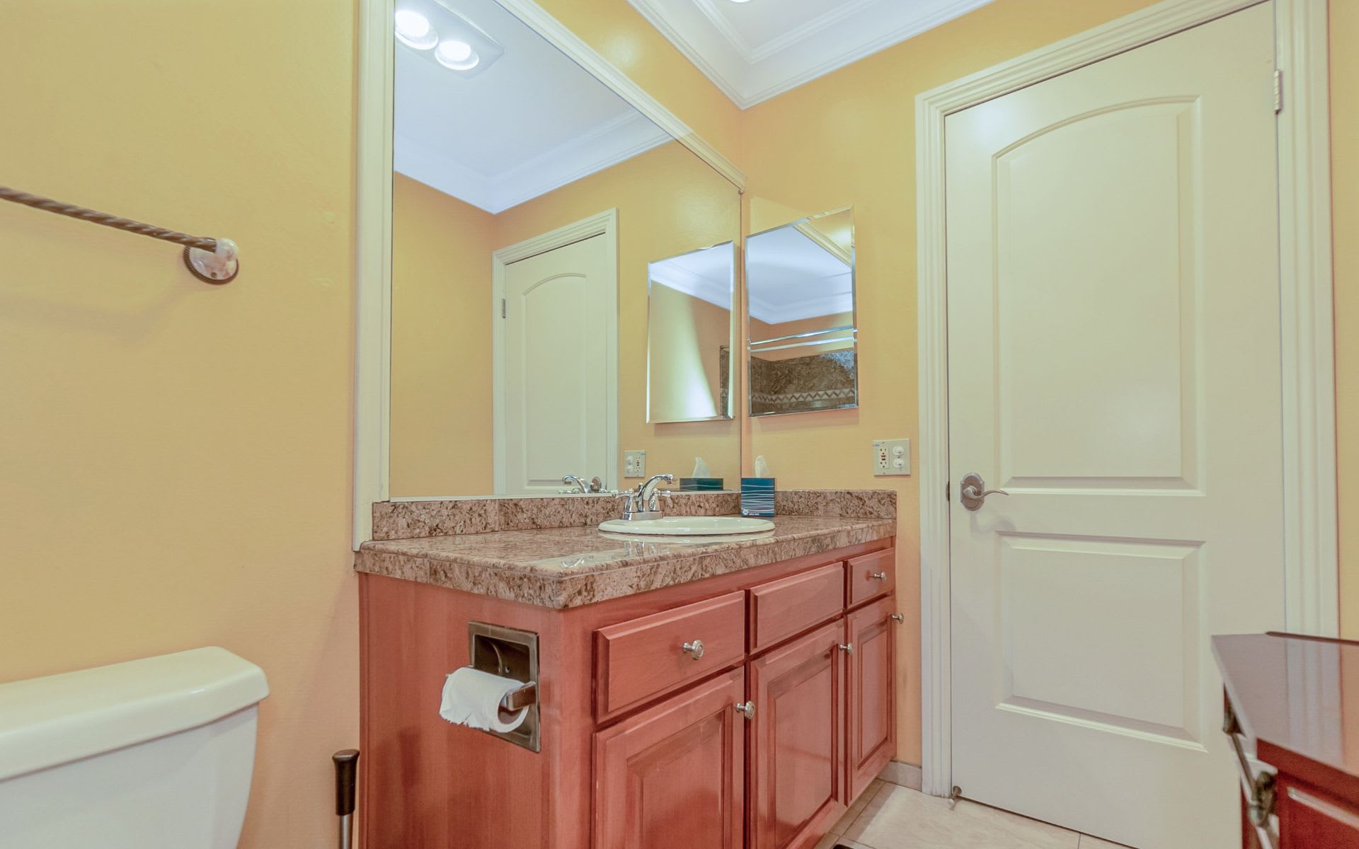 Bathroom with a reddish wood vanity, stone countertop, oval sink, and large mirrors.