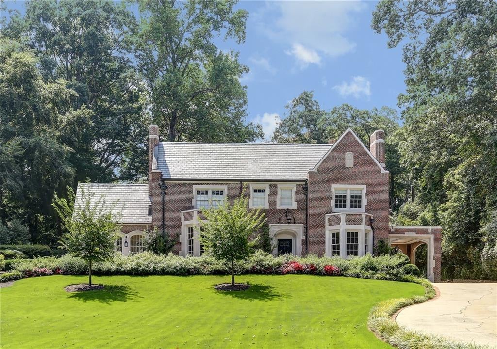 Two-story brick house with a lush lawn, a chimney, a covered porch, a 2-car garage, and a winding walkway.