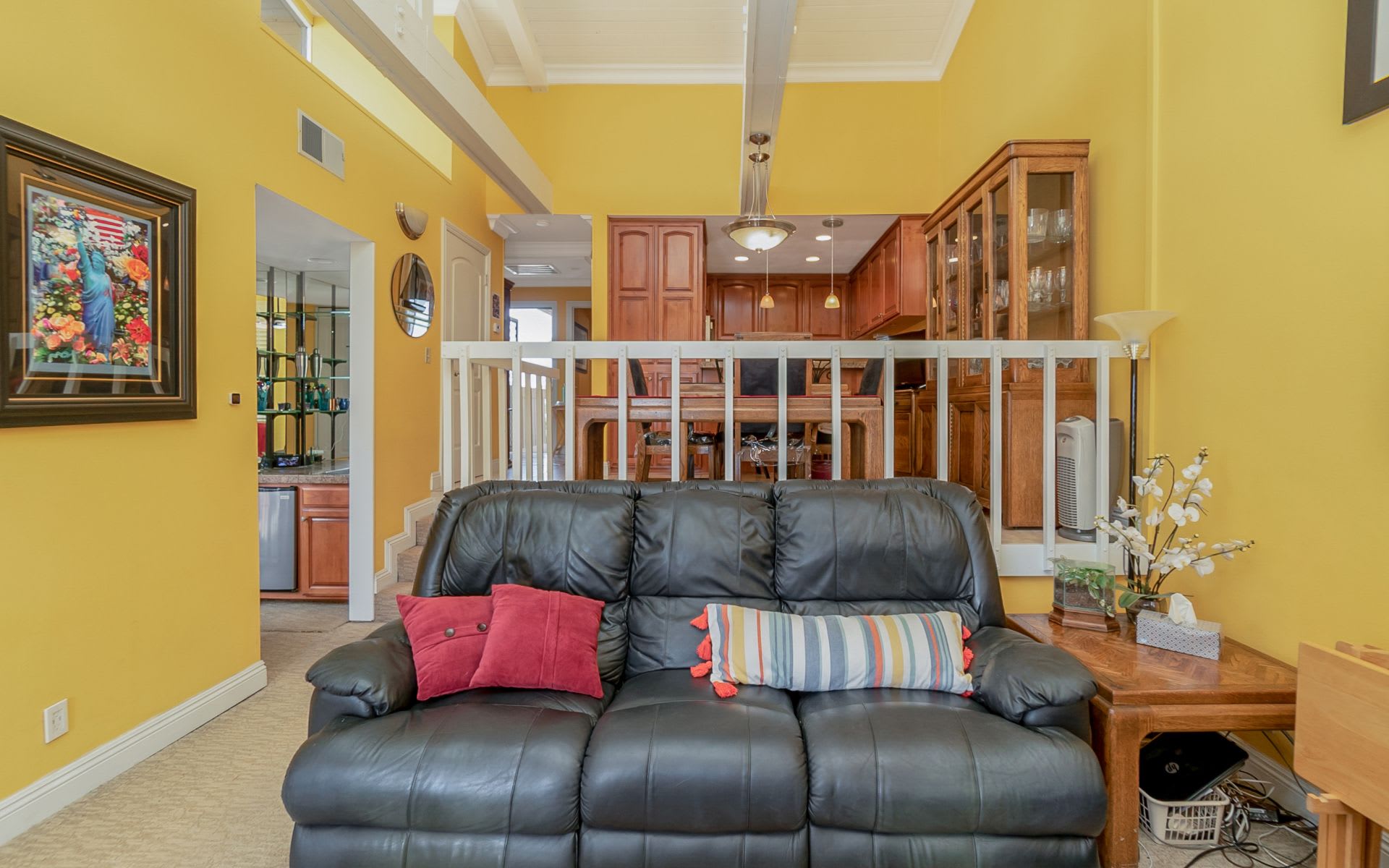 Living room with black leather sofa and yellow walls, opening to a wood-cabinet kitchen.