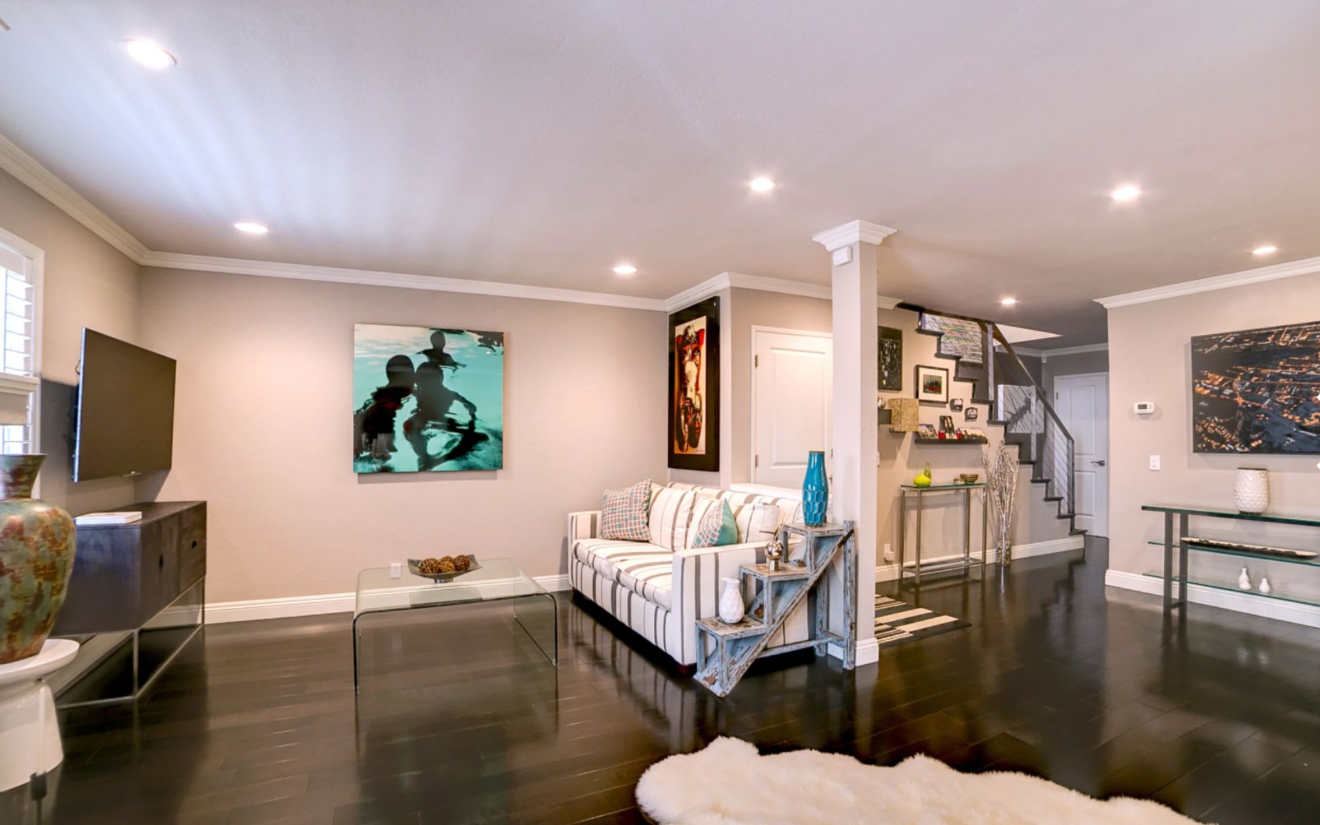 Living room with a striped sofa, dark hardwood floors, and a staircase.