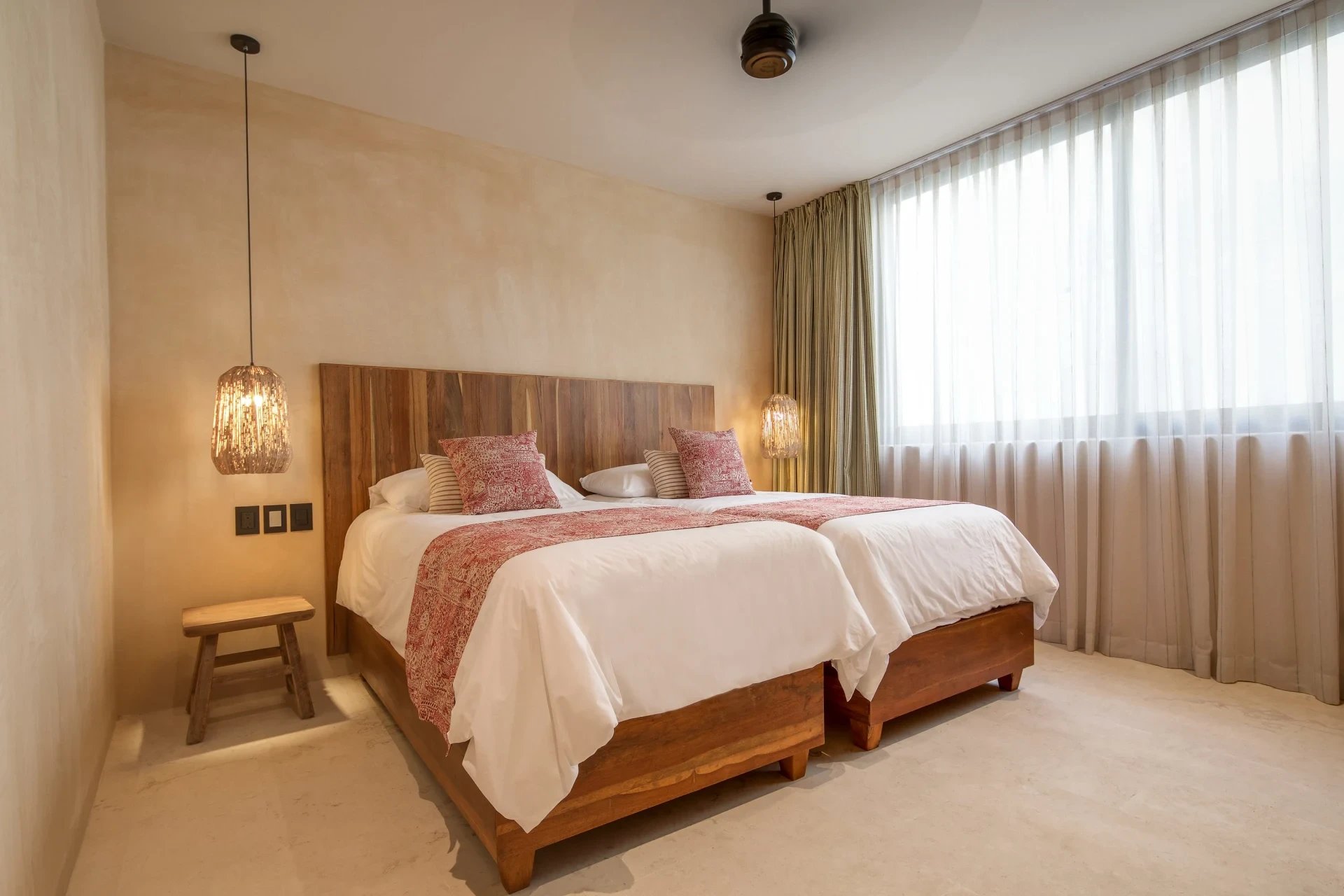Bedroom with two wooden beds, white linens, rose-patterned accents, and large curtained windows.