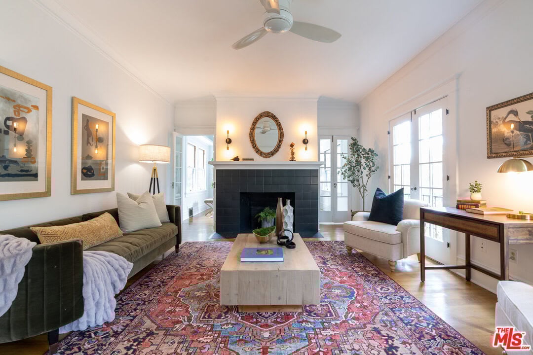 Bright living room with a dark fireplace, modern furniture, large windows, and a colorful patterned rug.