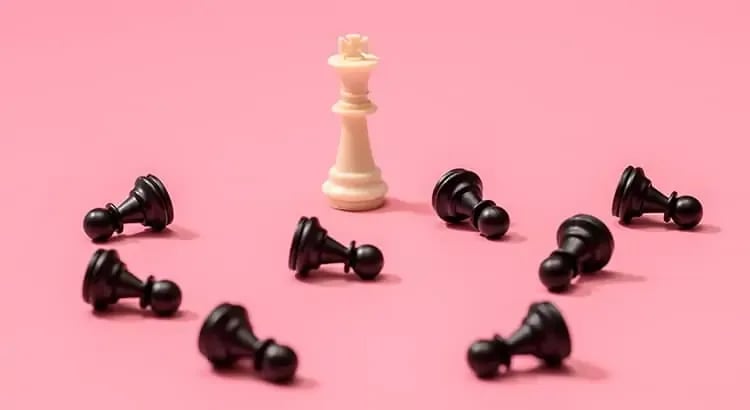 A chessboard with all black pawns except for one white queen, set against a pink background. This image likely symbolizes strategy, competition, or uniqueness.