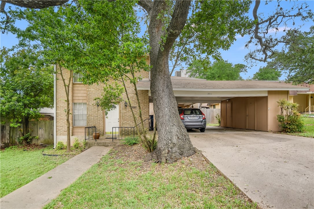 Two-story brick home with a mature tree in front and a covered carport beside the driveway.
