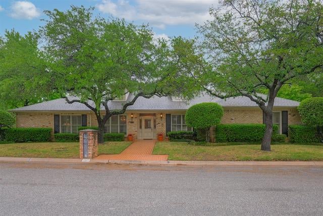 Single-story brick home with mature trees, trimmed hedges, and a brick walkway to the entrance.