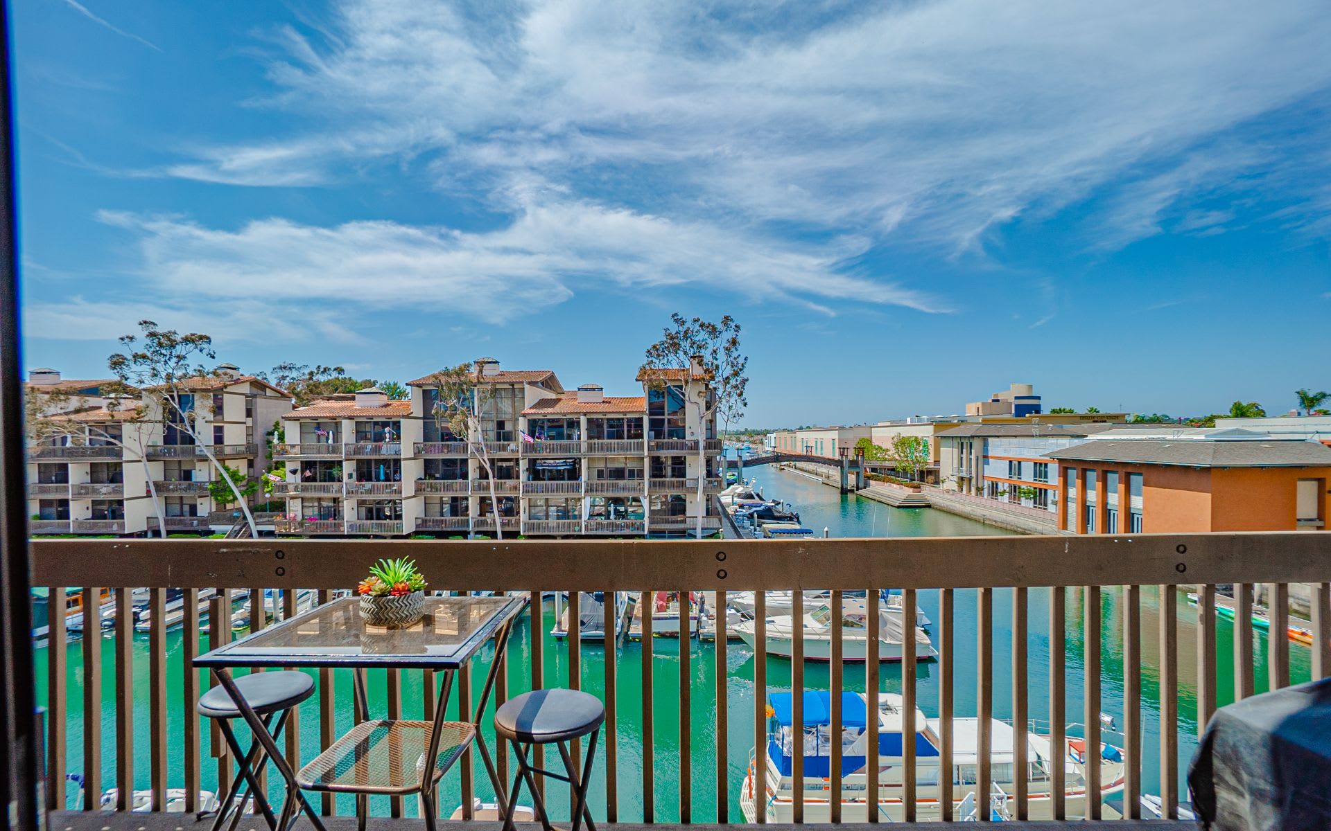 Furnished balcony overlooking a marina, with boats and waterfront buildings beyond the railing.