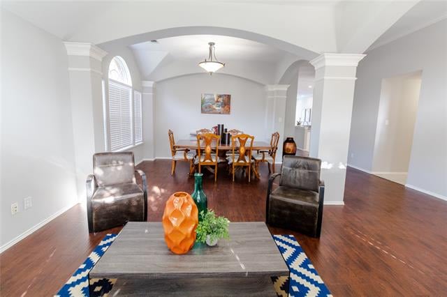 Open-plan living and dining area with dark hardwood floors, a wooden dining table, and arched ceiling.