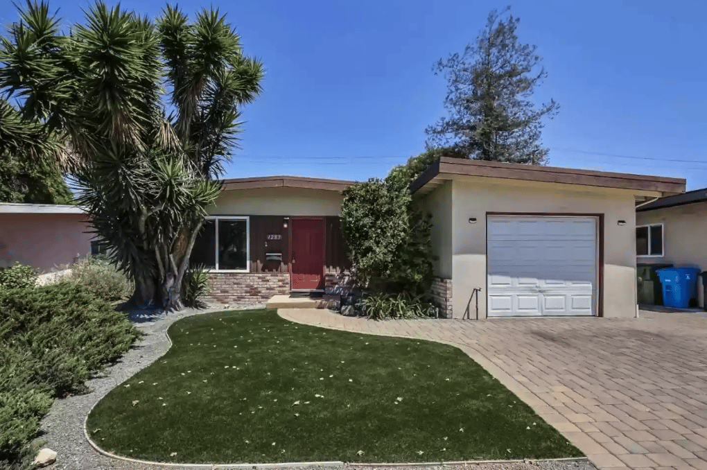 Single-story home with a red front door, attached garage, and curved lawn among drought-tolerant landscaping.