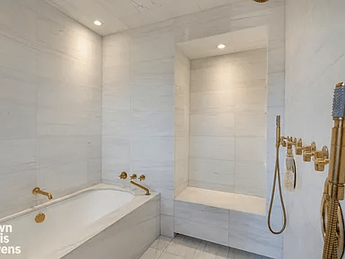 Marble-tiled bathroom with a built-in bathtub and polished brass shower fixtures.