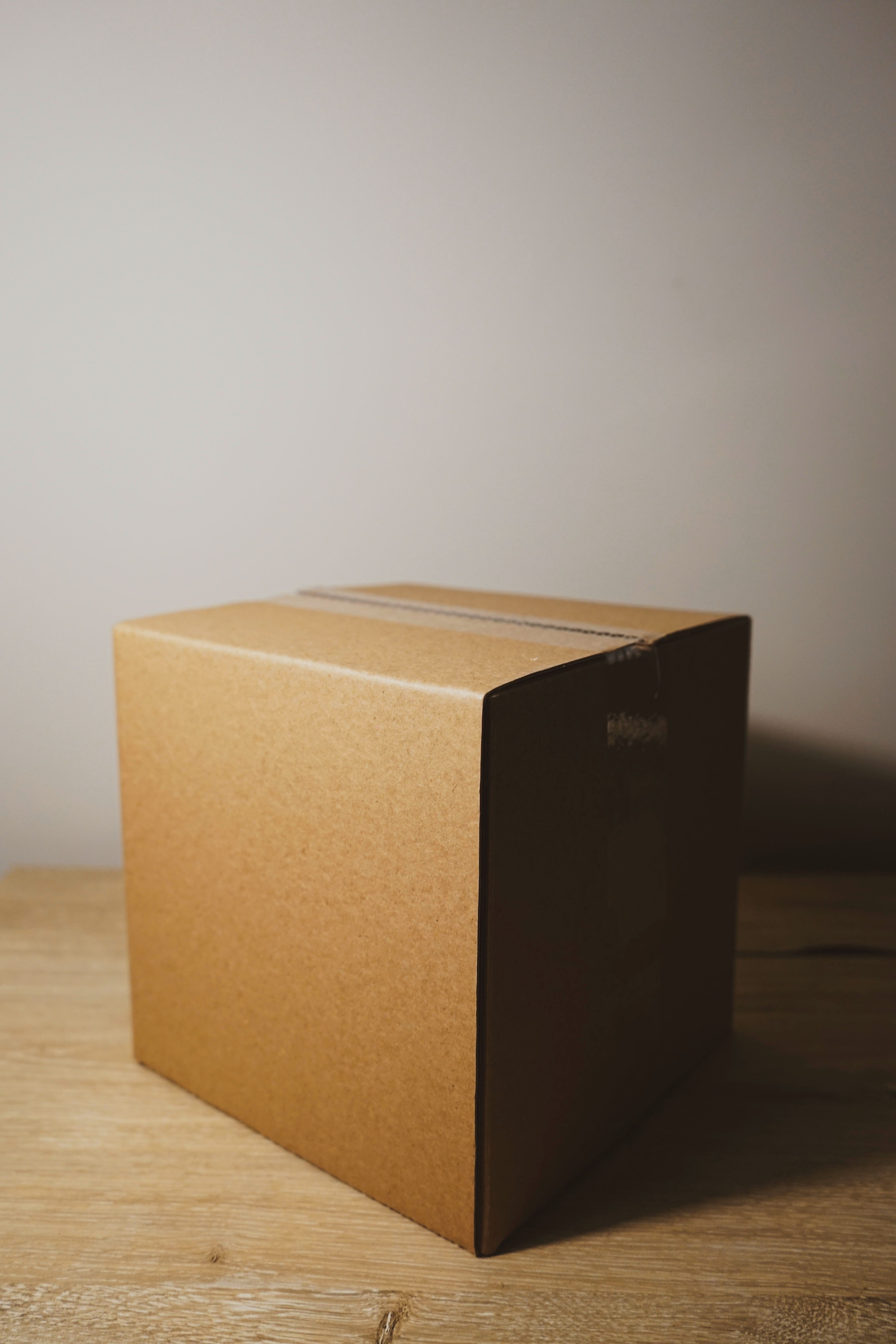 Sealed cardboard moving box on a wooden floor, with its right side in shadow.