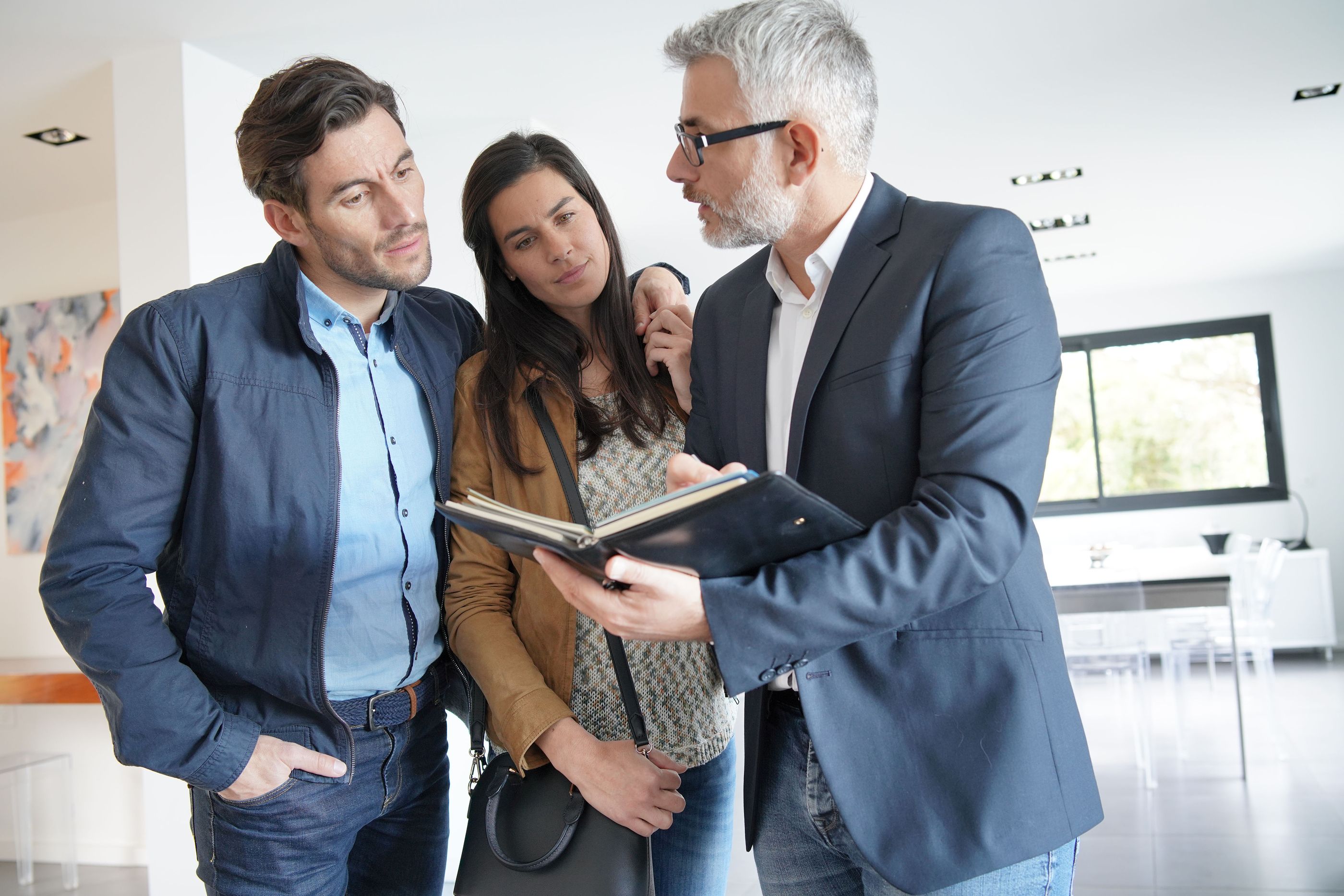 Real estate agent reviews a portfolio with a couple in a bright modern home.