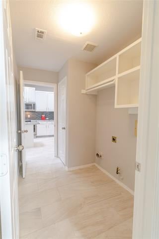 Empty laundry room with upper storage shelves, washer and dryer hookups, and light tile flooring.