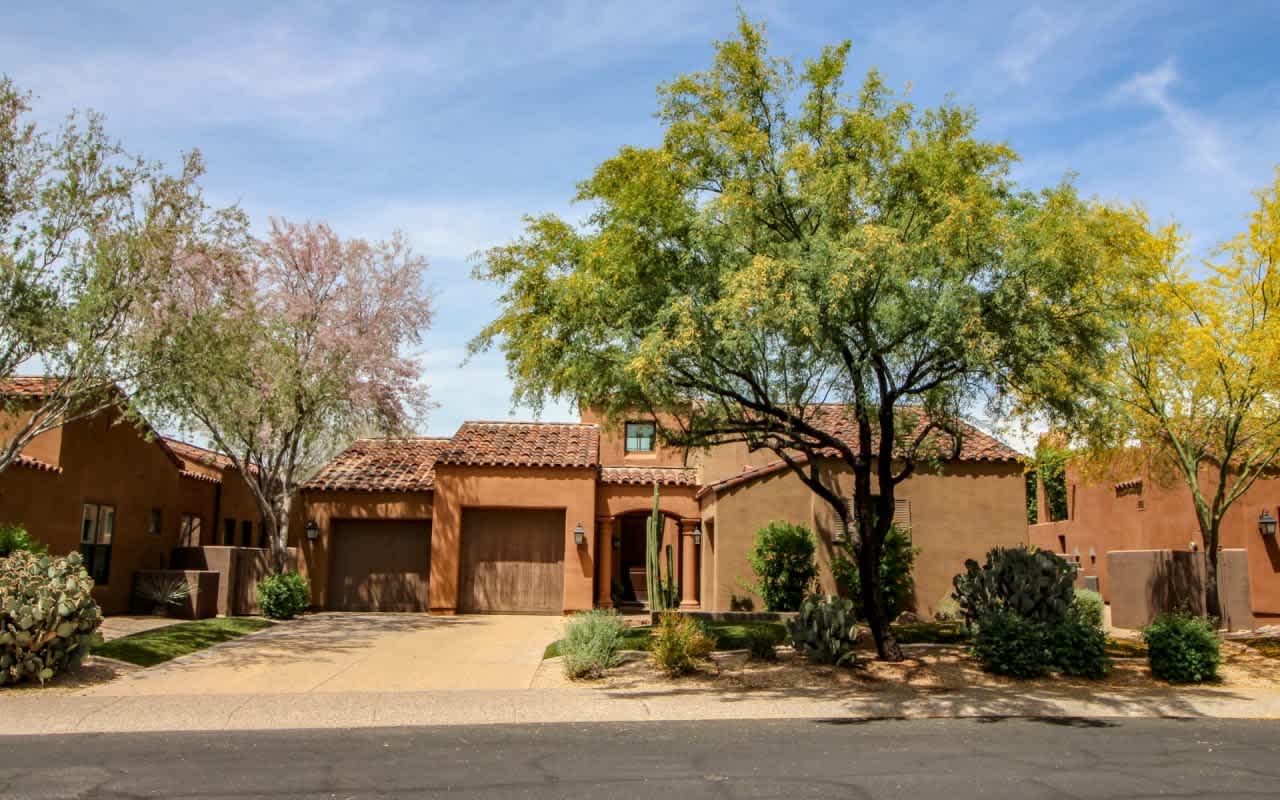 Mediterranean-style luxury home with terracotta roof, arched entry, and lush landscaping, ideal for a tranquil oasis.