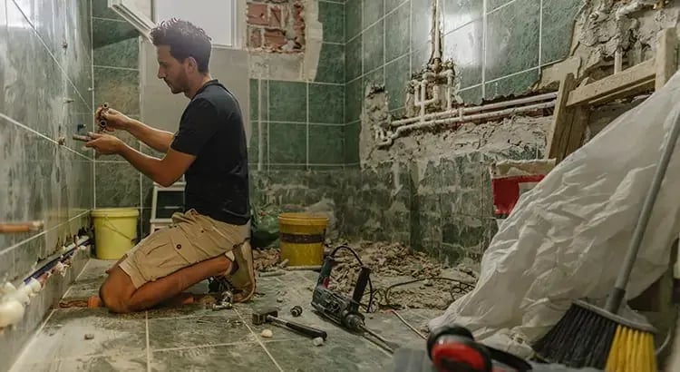 A man working on a renovation project in a bathroom. The room appears to be under construction, with tools and materials scattered around.