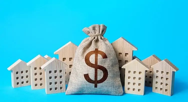 A burlap sack with a dollar sign on it, surrounded by small house models. This image represents real estate investment or financial planning.