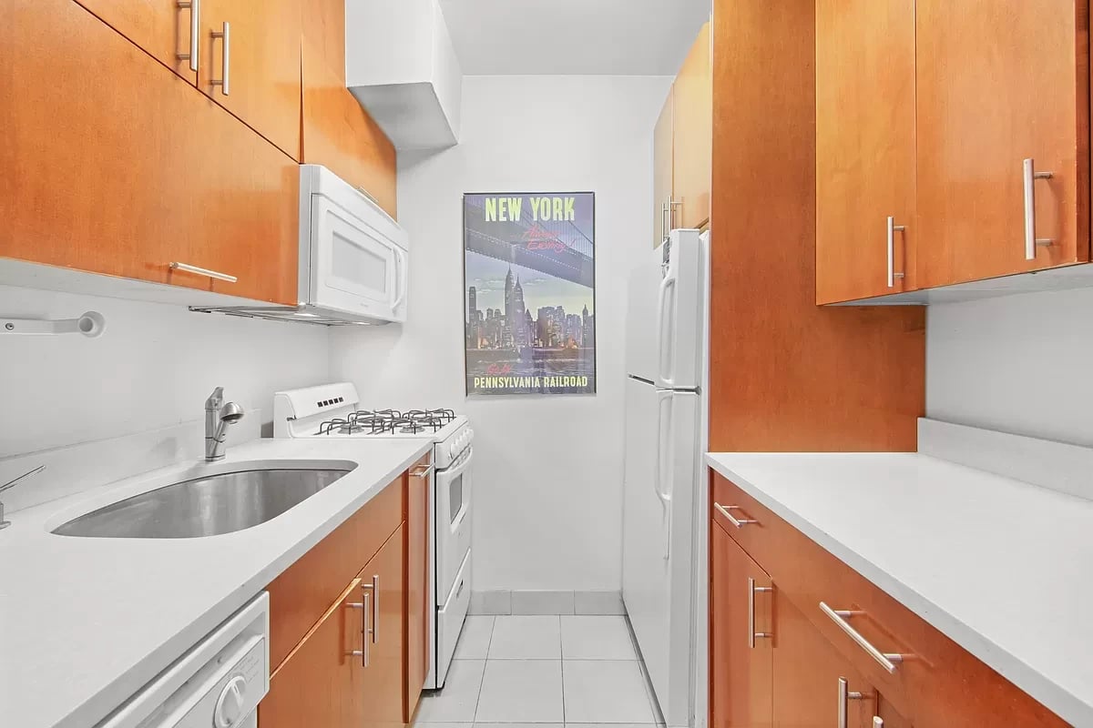 Narrow apartment kitchen with warm wood cabinets, white countertops, and a New York poster.