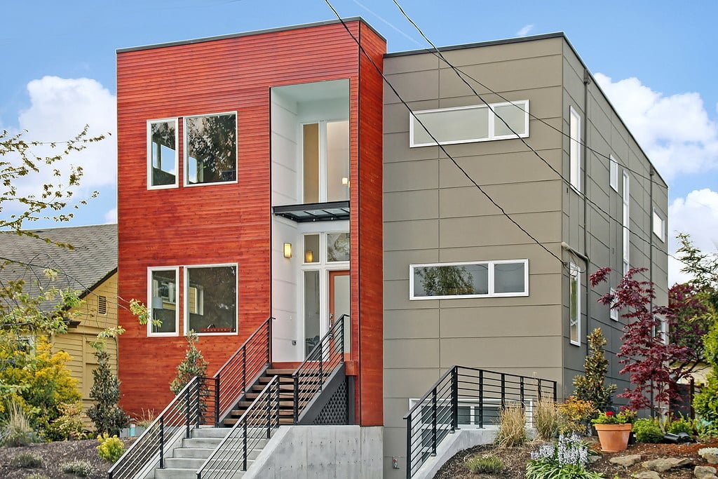 Modern Seattle home with red wood siding, gray facade, and front stairs with black railings.