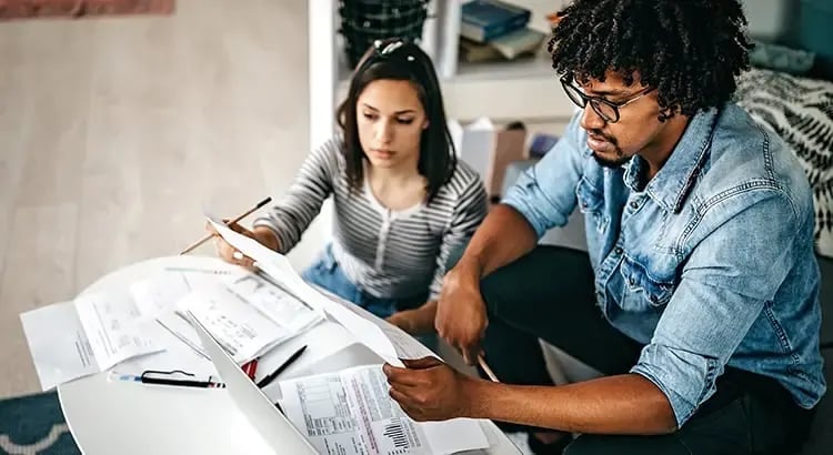 A couple reviewing documents together at a table. They appear to be discussing financial matters or paperwork related to home buying.