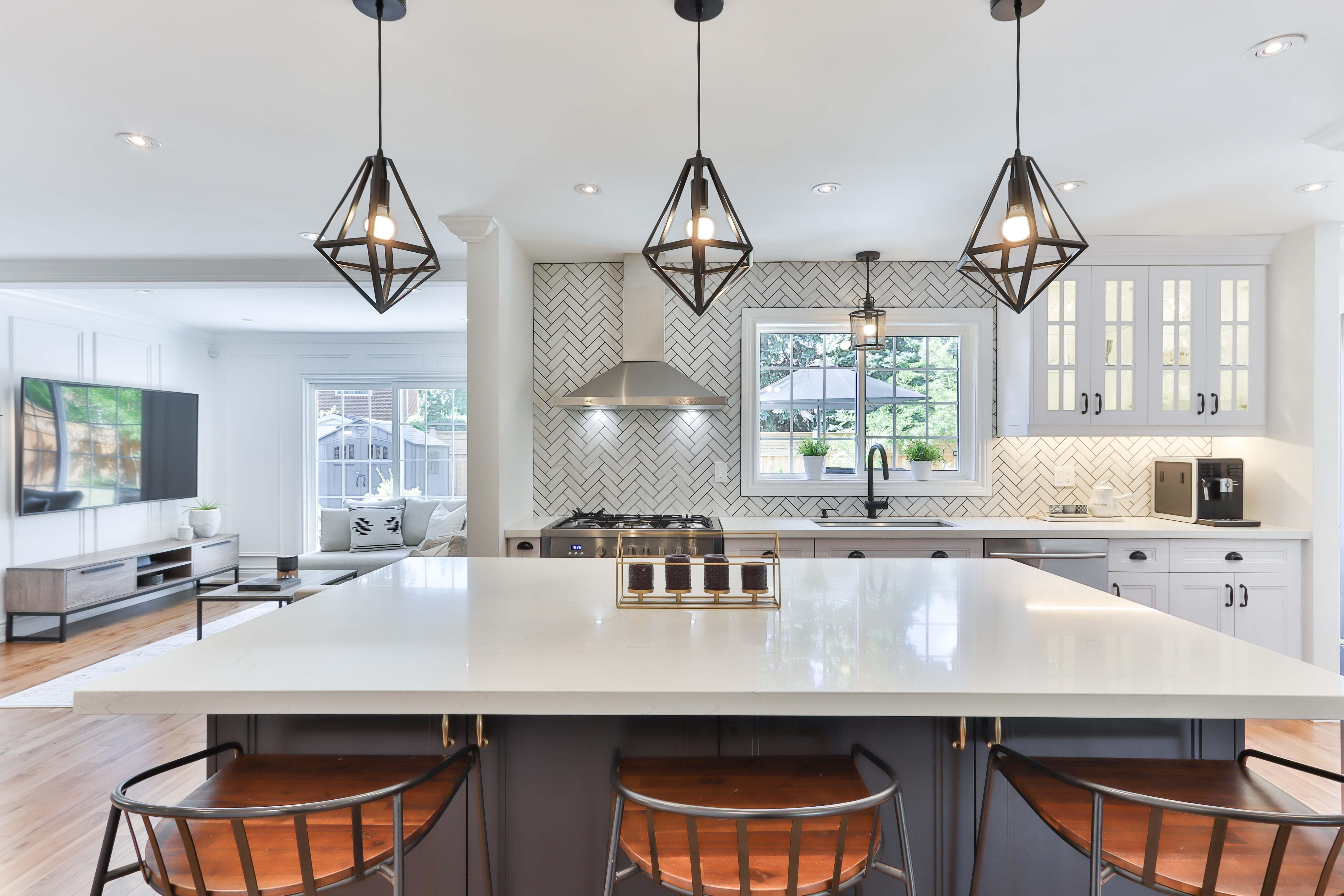 Open-plan kitchen with a large island, geometric pendant lights, and herringbone tile backsplash.