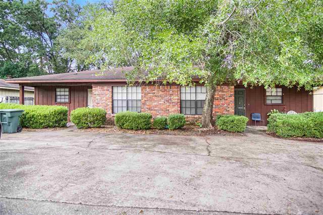 A multi-family brick house in 2857 and 2859 Mission Rd with a large driveway and a well-maintained front yard. The yard features several shrubs and a large tree providing shade.