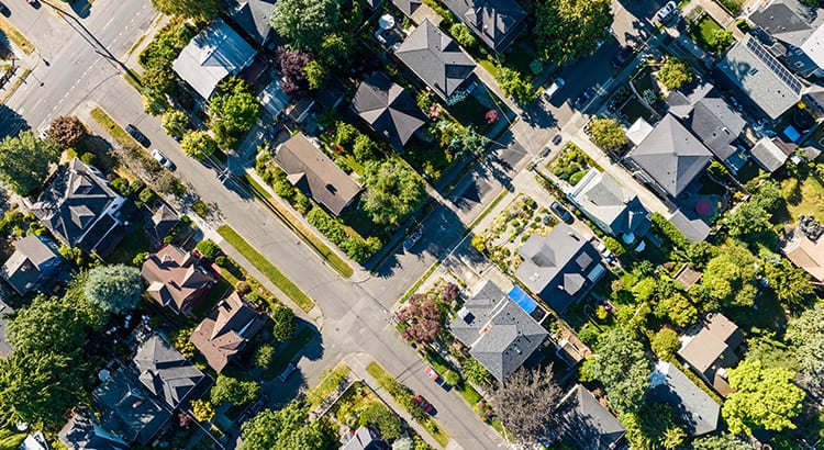 An aerial view of a neighborhood, showcasing several houses with yards and tree-lined streets. This image provides a broader perspective of the area, highlighting the layout and density of the housing development.