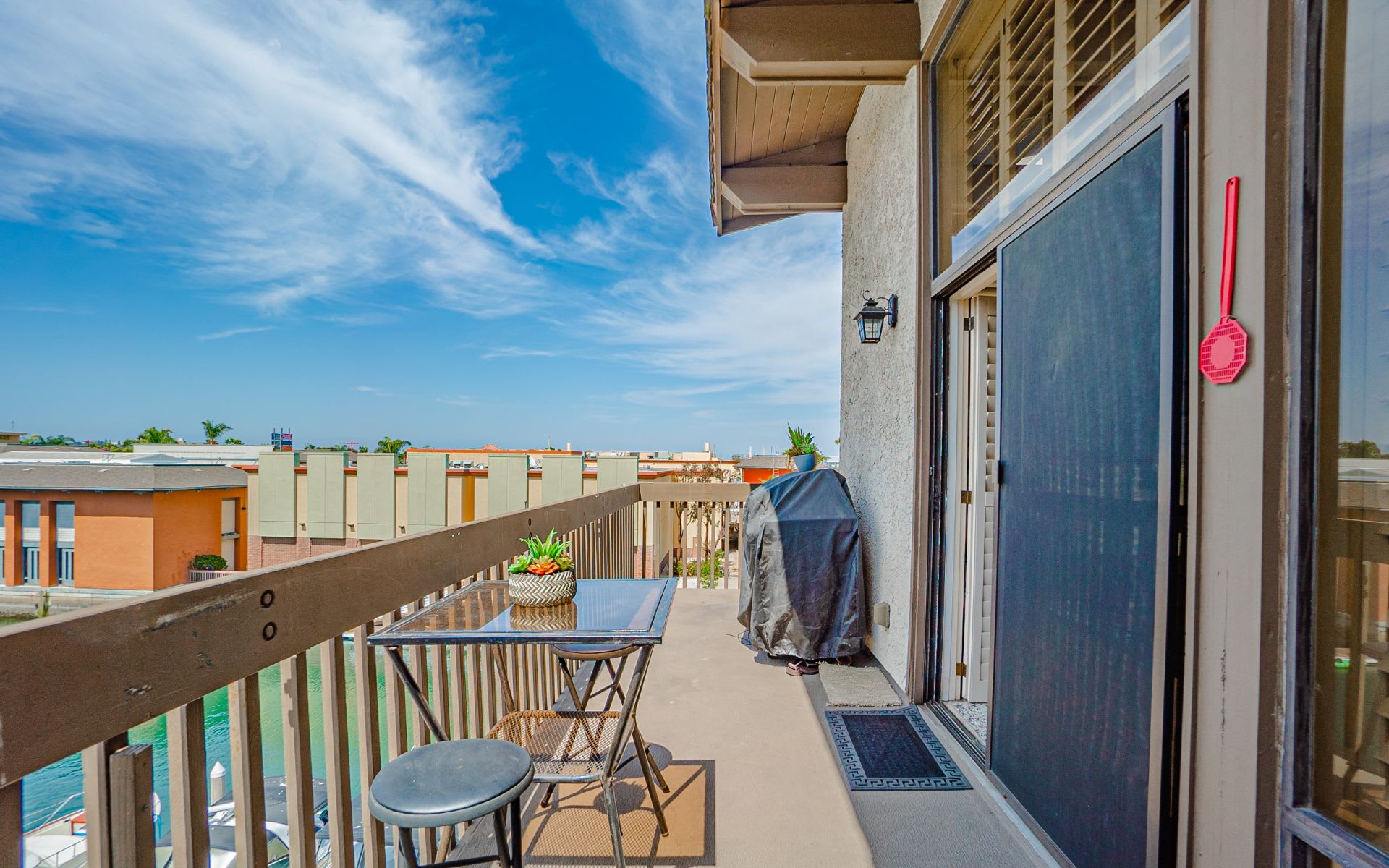 Apartment balcony with outdoor dining set and grill overlooking water and neighboring buildings.