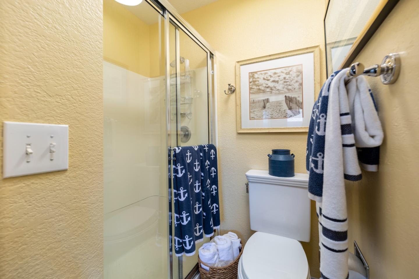 Bathroom with a glass shower, white toilet, and navy anchor-patterned towels.