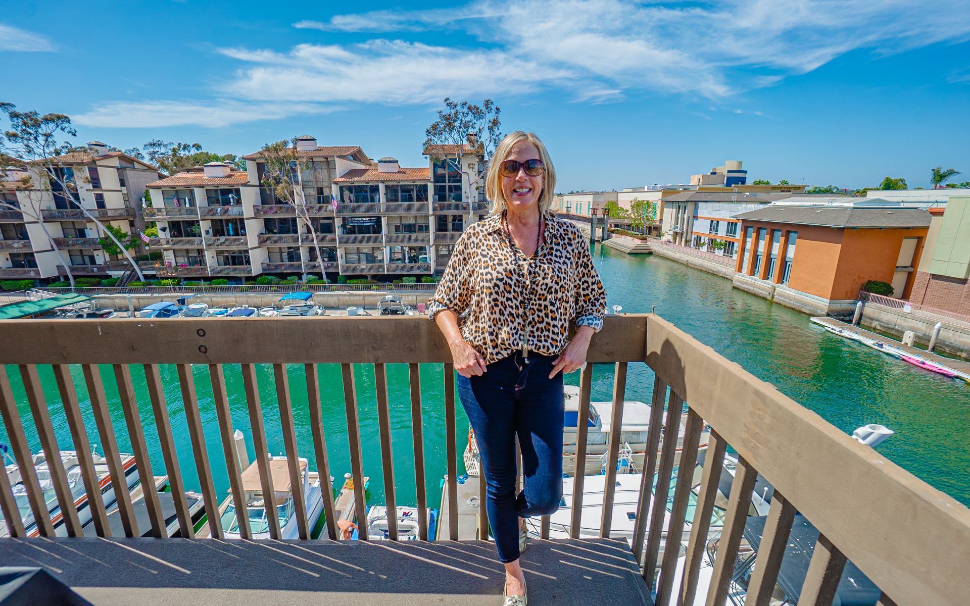 Balcony overlooking a marina, with a woman by the railing and condominium buildings across the water.