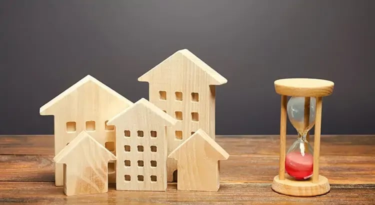 Wooden house models of various sizes next to an hourglass. This image likely represents real estate, time, or investment.