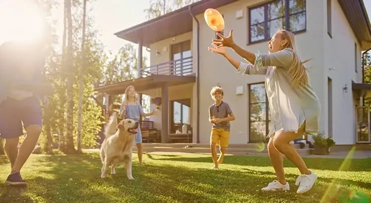 A family playing with a dog in the yard of a two-story house, showcasing family life and outdoor living space.