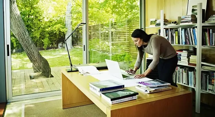 A person working at a desk in a home office or library. The environment is bright and filled with books, indicating a productive workspace.