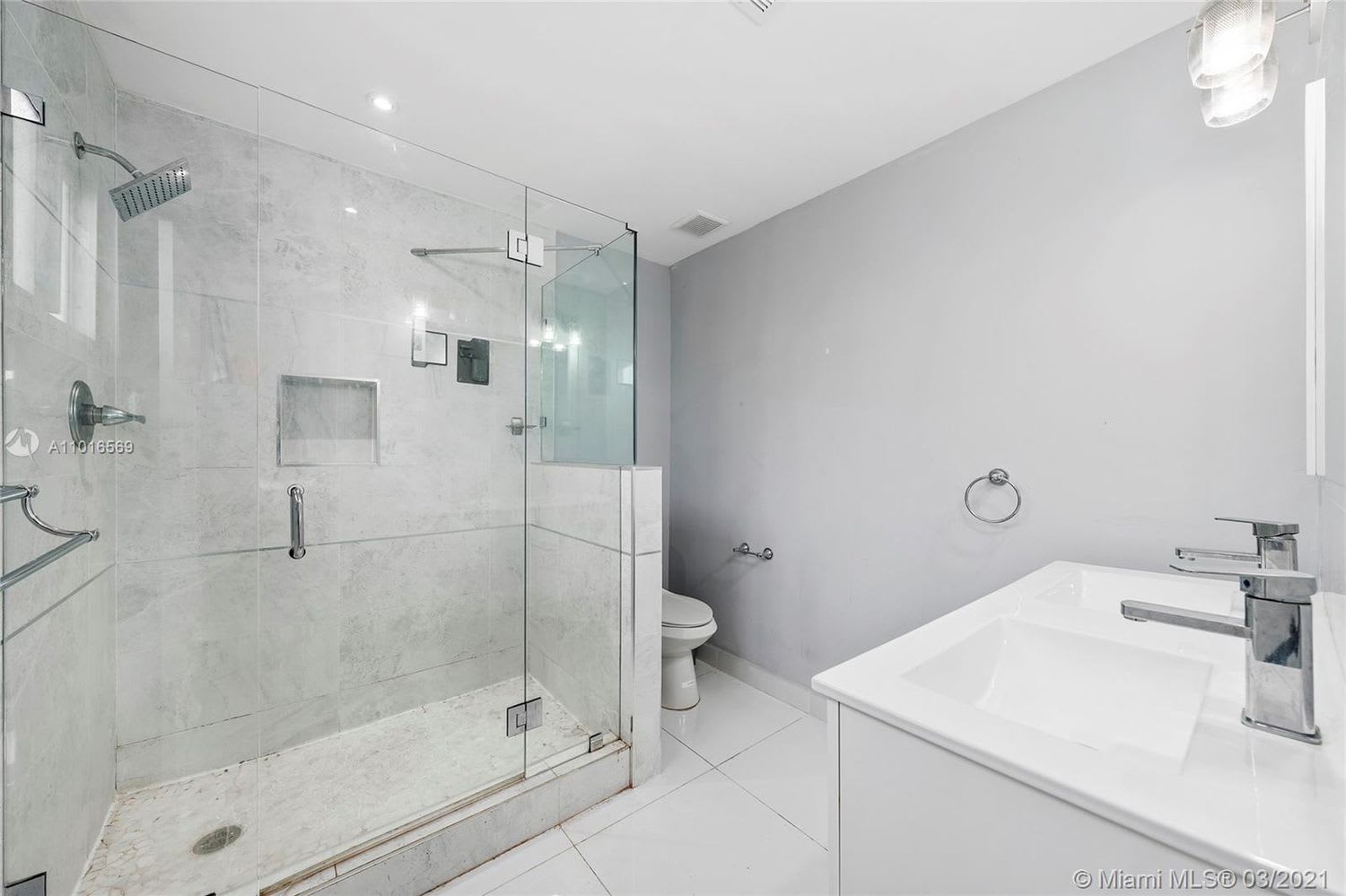 Modern bathroom with a glass-enclosed marble-tile shower and white vanity.