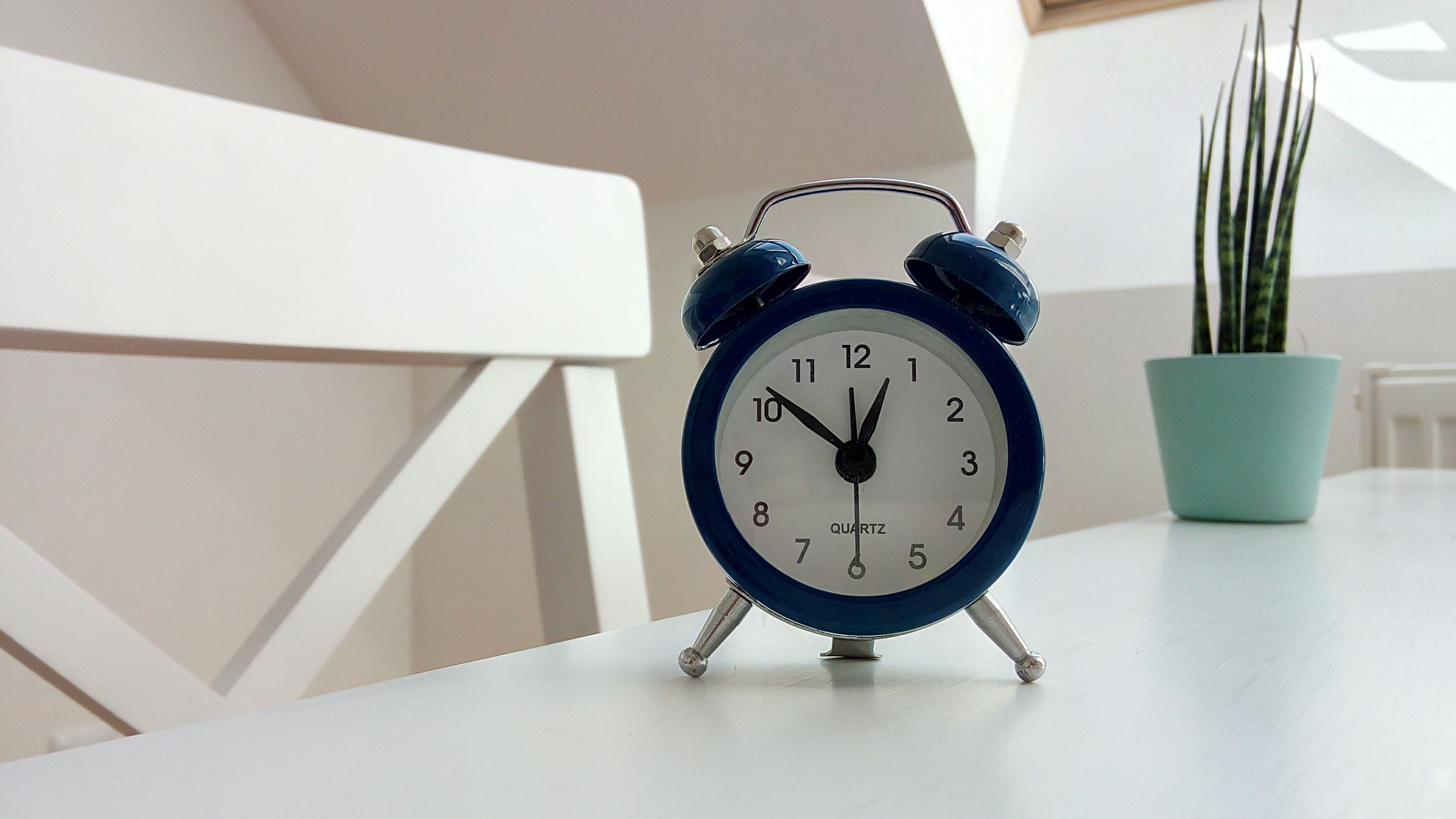 Navy blue twin-bell alarm clock on a white tabletop beside a potted plant.