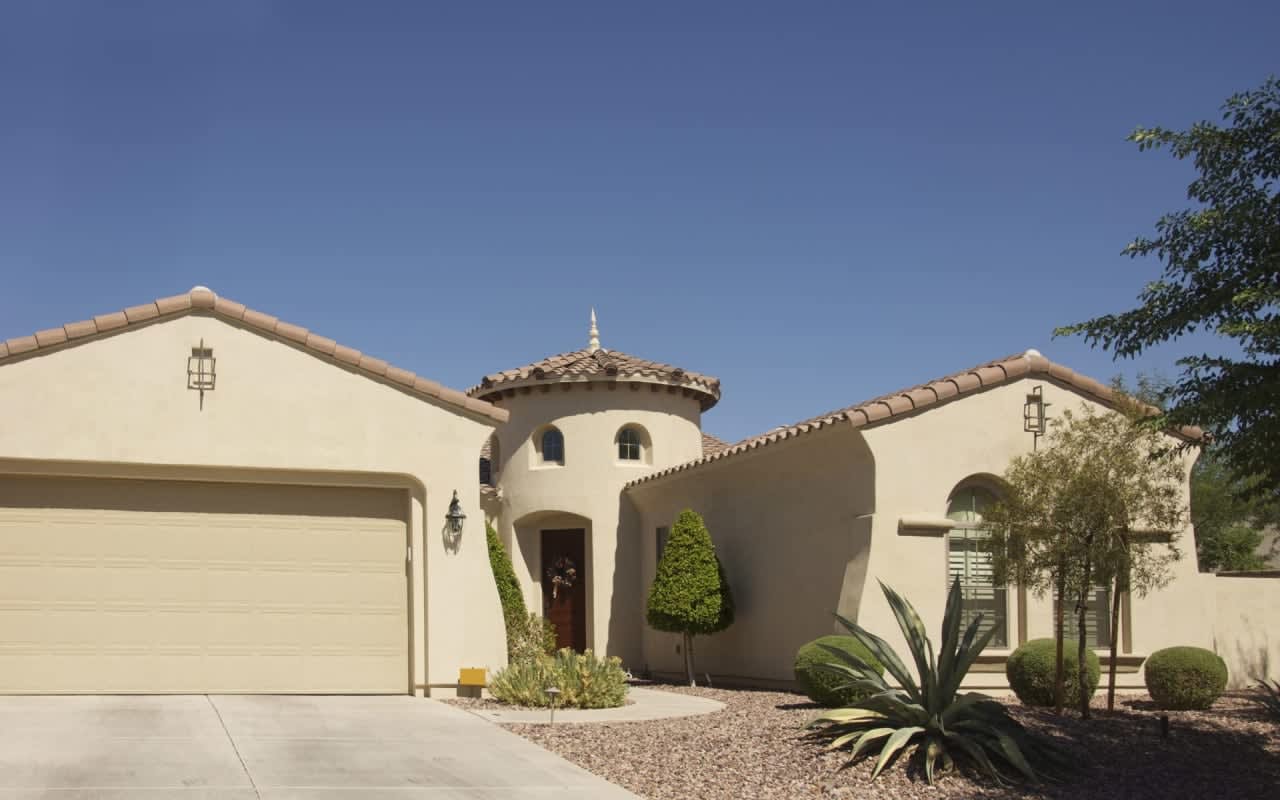 Tuscan-style stucco home with terracotta roof and arched windows offers luxury family living in a lush palm-tree setting.