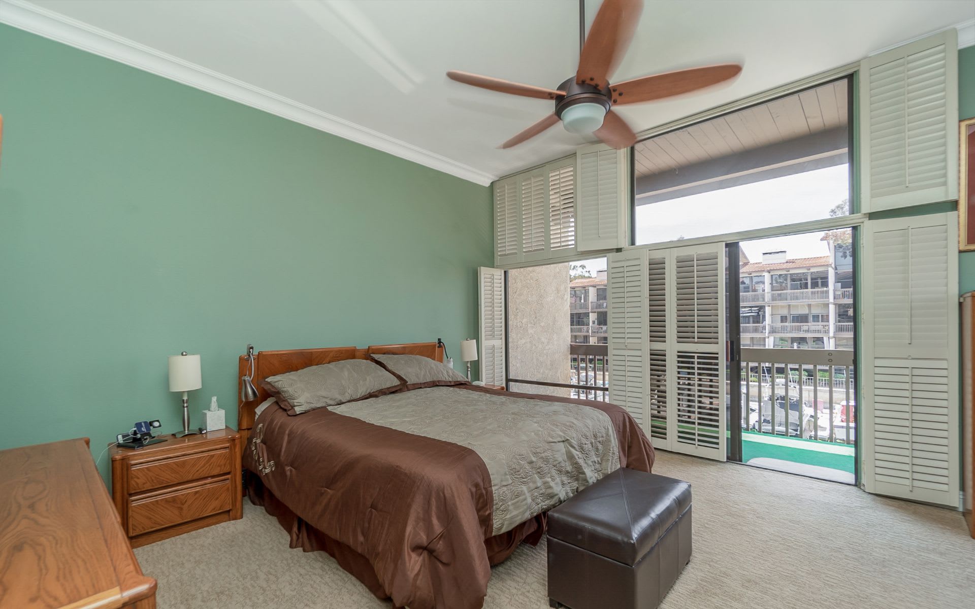 Bedroom with a ceiling fan, louvered shutters, and tall windows opening onto a balcony.