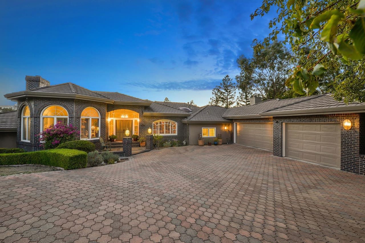 Brick home with arched lit windows, a wide paver driveway, and two garage doors.